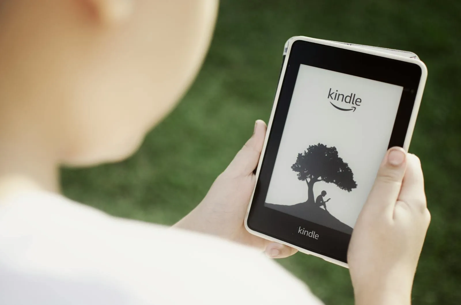 Criança com chapéu de sol a segurar um Kindle Paperwhite no jardim, com relva ao fundo