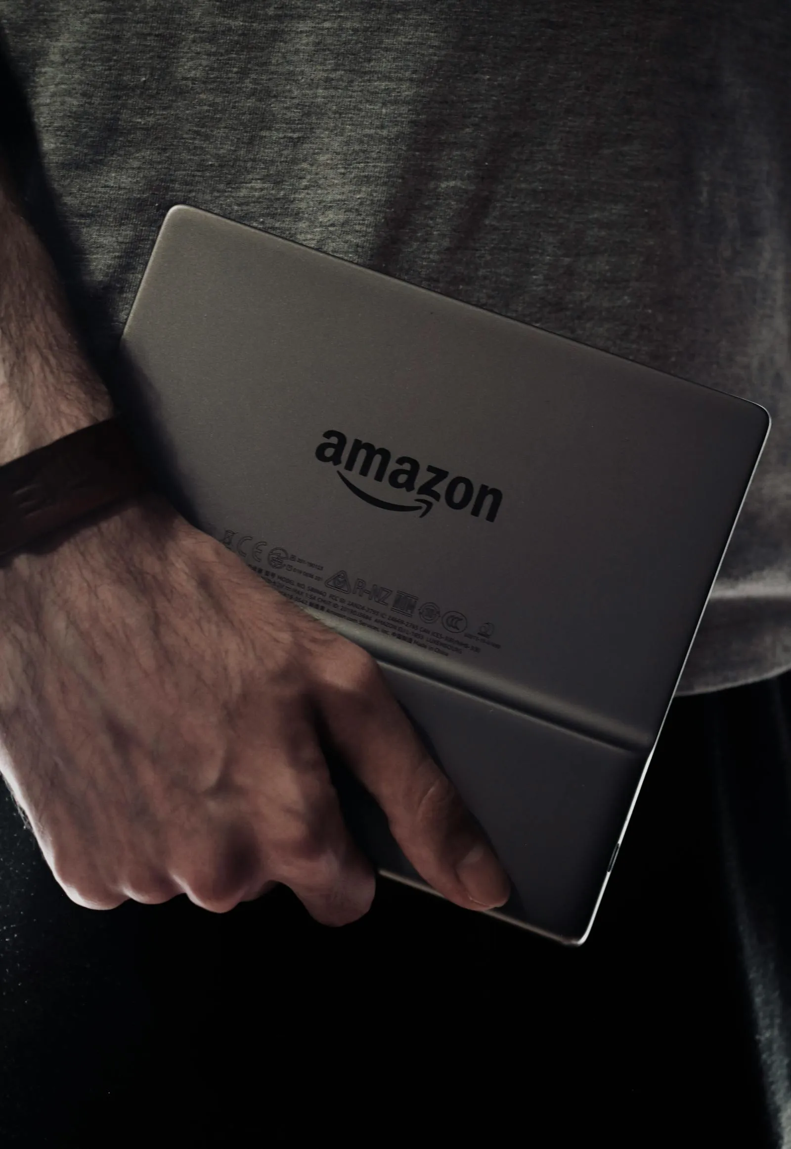 Vista da traseira de um Kindle com o logótipo Amazon, segurado numa mão